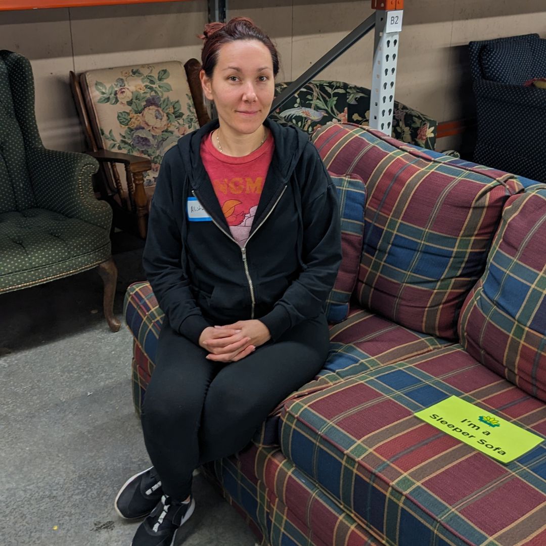 Alisha sits smiling on a plaid red, blue, and green couch