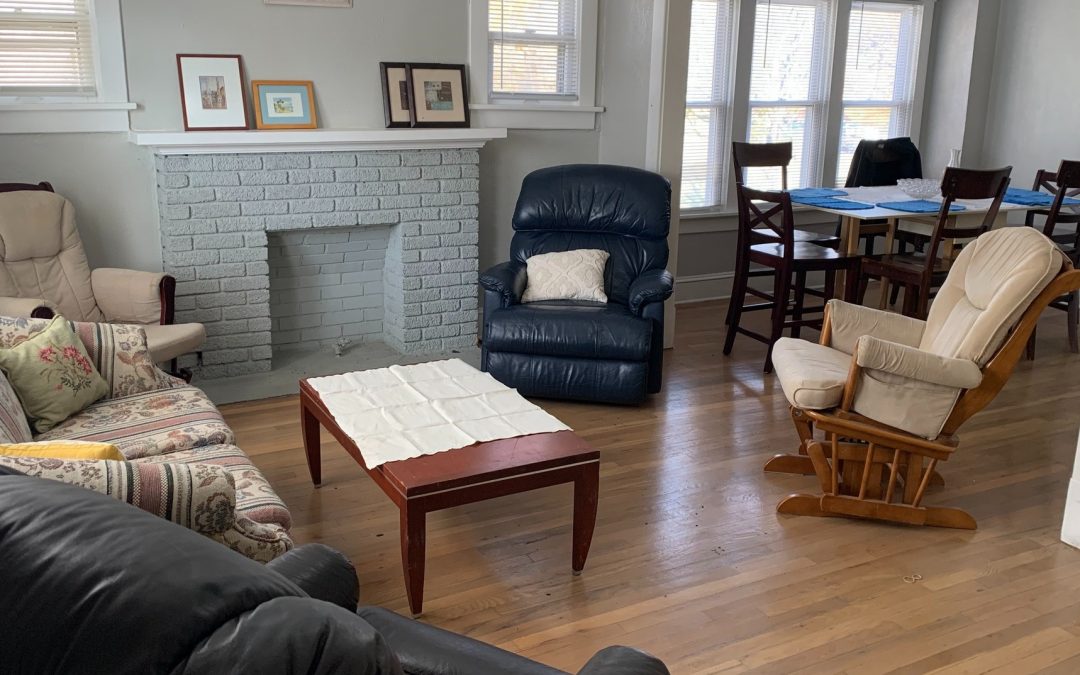 Living room with armchairs, coffee table, pictures on the wall, and a dining room table with chairs and bowls and placemats in the background