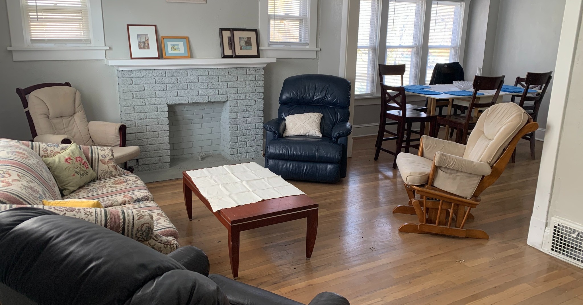 Living room with armchairs, coffee table, pictures on the wall, and a dining room table with chairs and bowls and placemats in the background