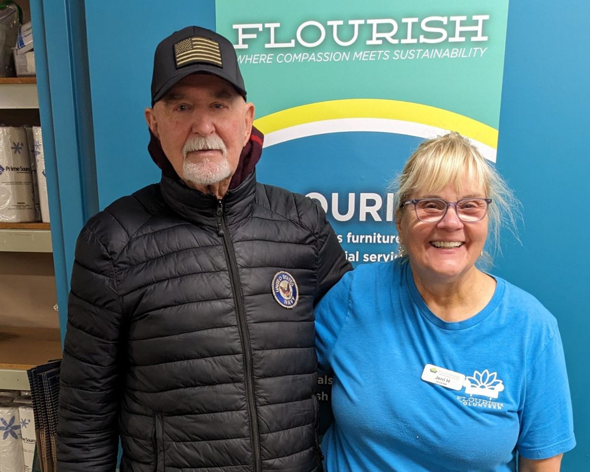 Jerry, guest, and Jerri, Flourish volunteer, pose in front of Flourish sign