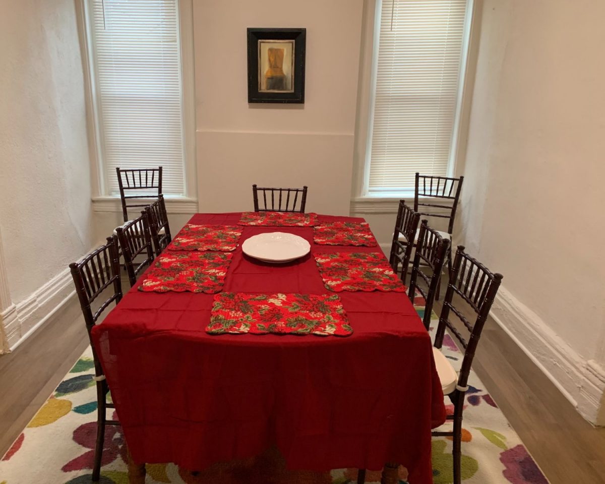 Dining room table set with bright red table cloth and set of matching dishes with a rug underneath and a picture on the wall